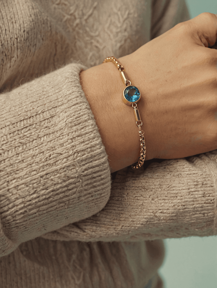 Gold bracelet with a blue gemstone worn on a wrist