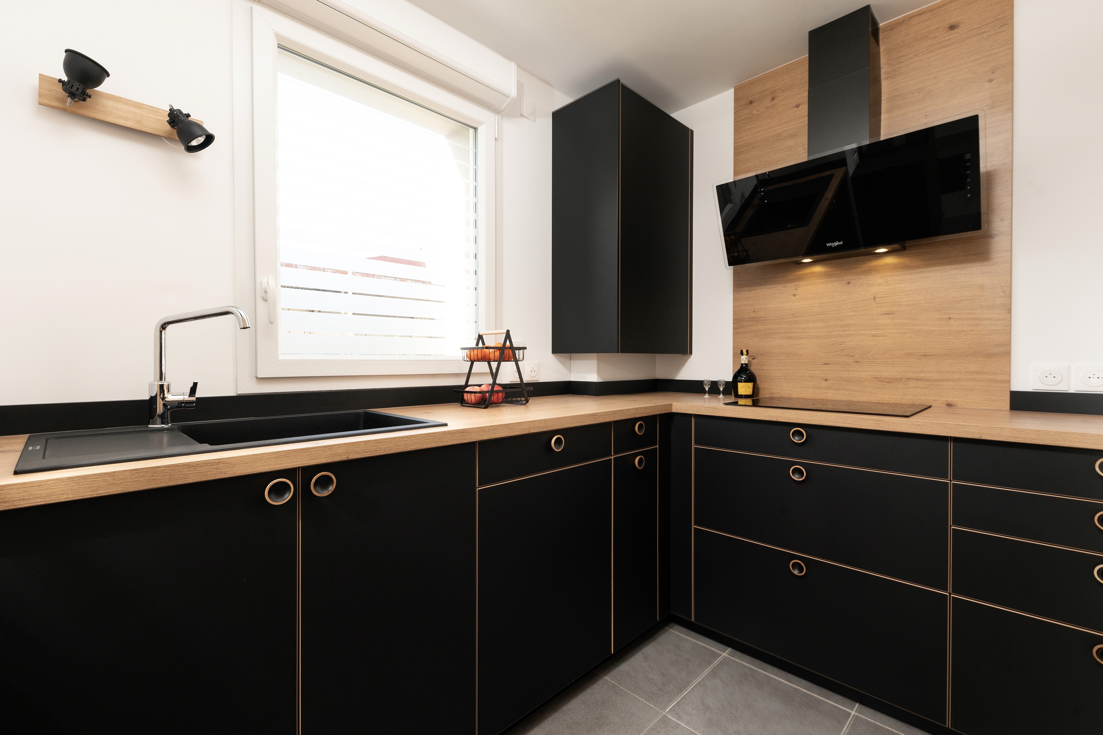 Transformation cuisine 77 avec armoires noires, comptoirs bois, évier noir sous fenêtre et décor minimal, architecte d'intérieur clé en main.