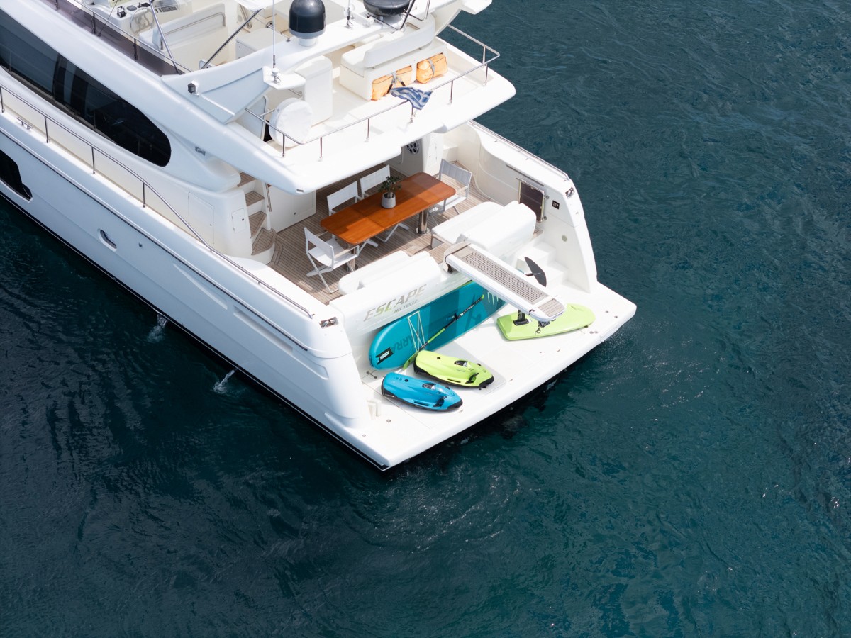 White Ferretti 63 motor yacht anchored in turquoise waters with water toys on the swim platform and outdoor dining area on deck.