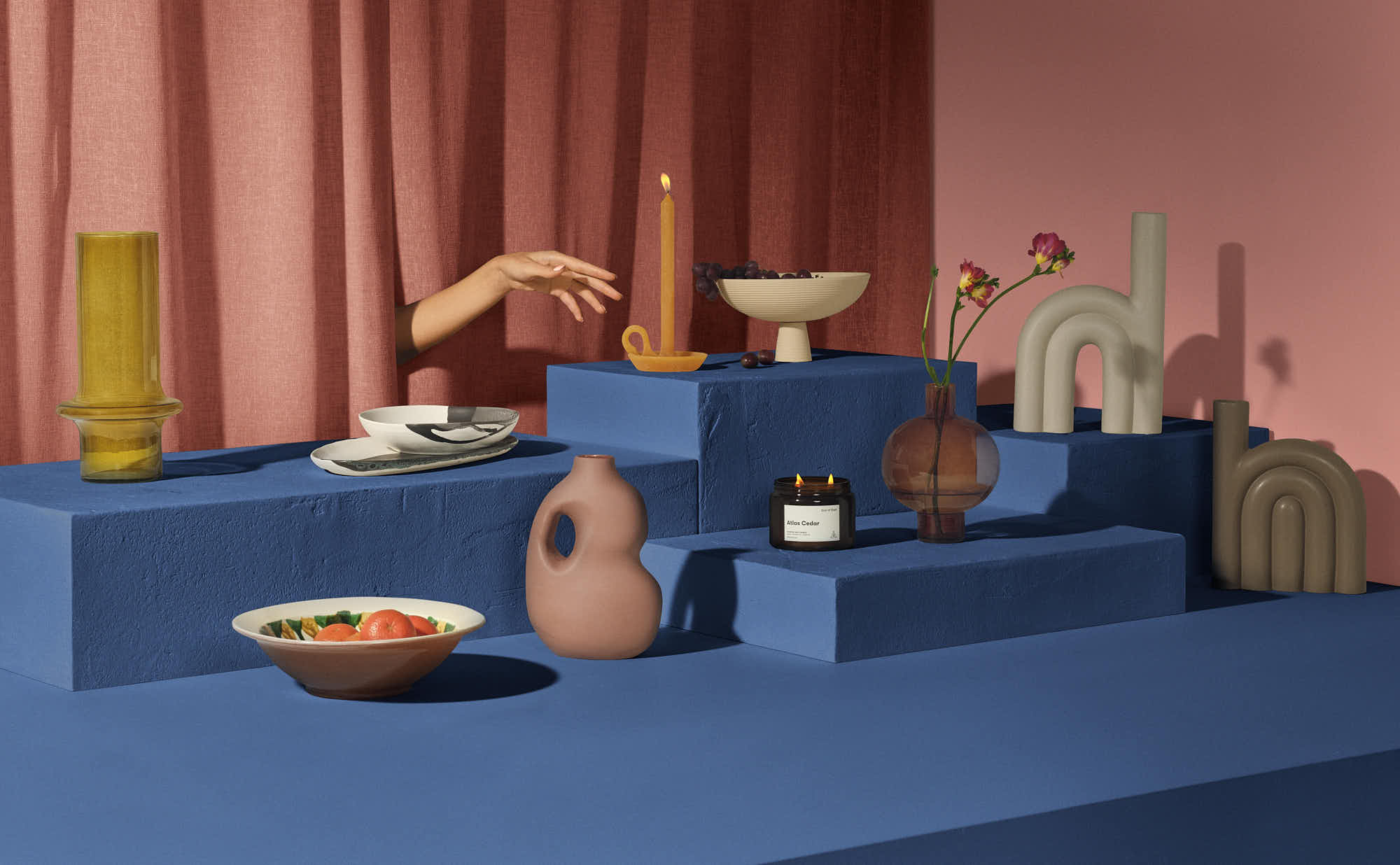 Modern minimalist home decor setup with candles, vases, and geometric shapes on blue blocks.