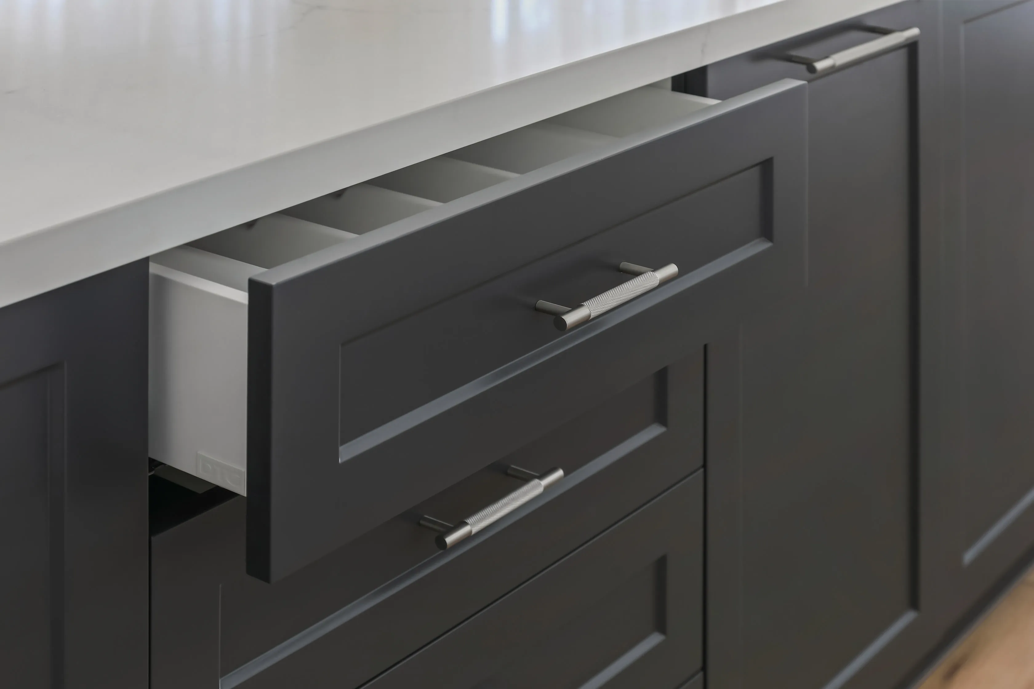 Open drawer detail in the charcoal shaker island, showing knurled nickel bar handles, a cutlery insert and white stone benchtop