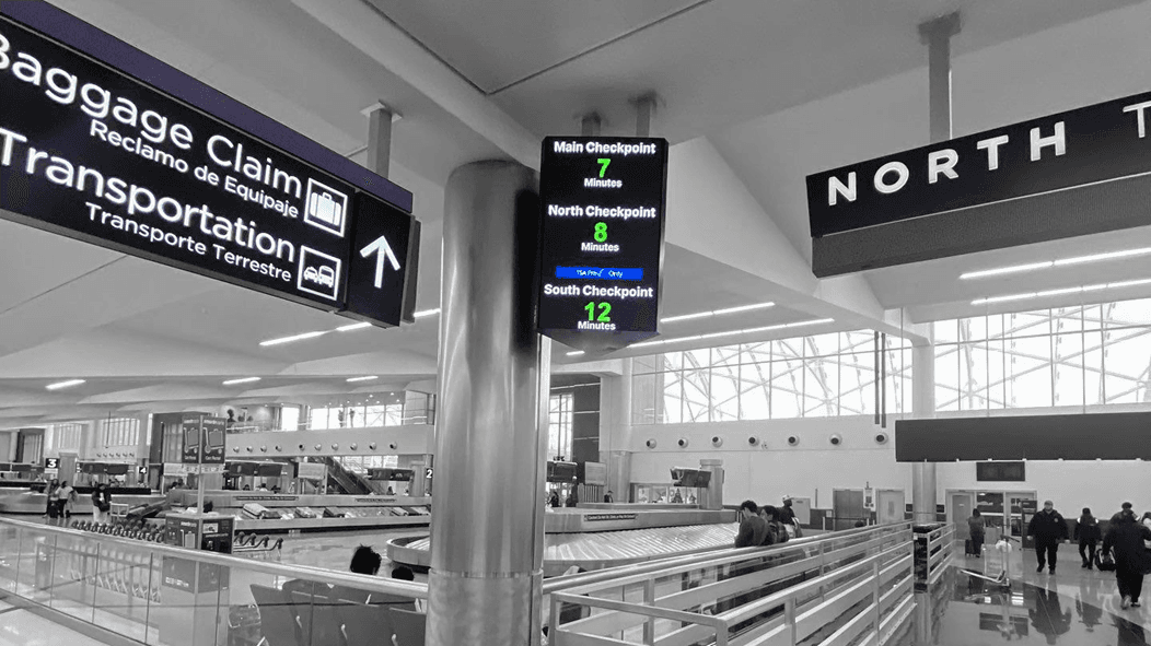 A photo of multiple digital signs in an airport, including a live security time update screen