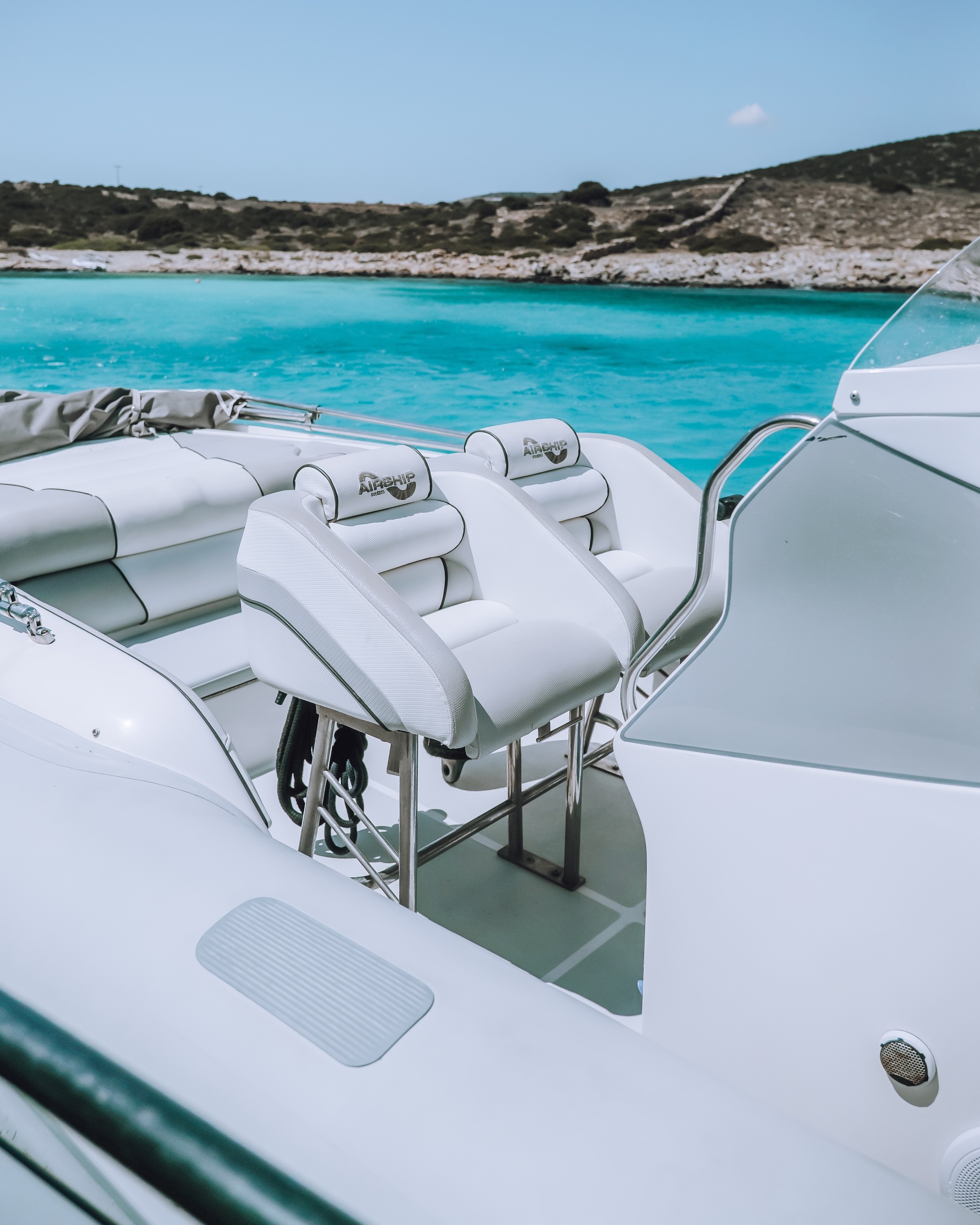 White captain's chairs on Airship 30 yacht deck with turquoise waters and rocky Cycladic coastline in background.