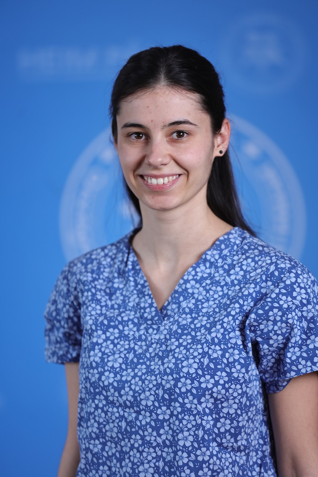 Mosolygós hosszúhajú nő kék virágmintás orvosi ruhában