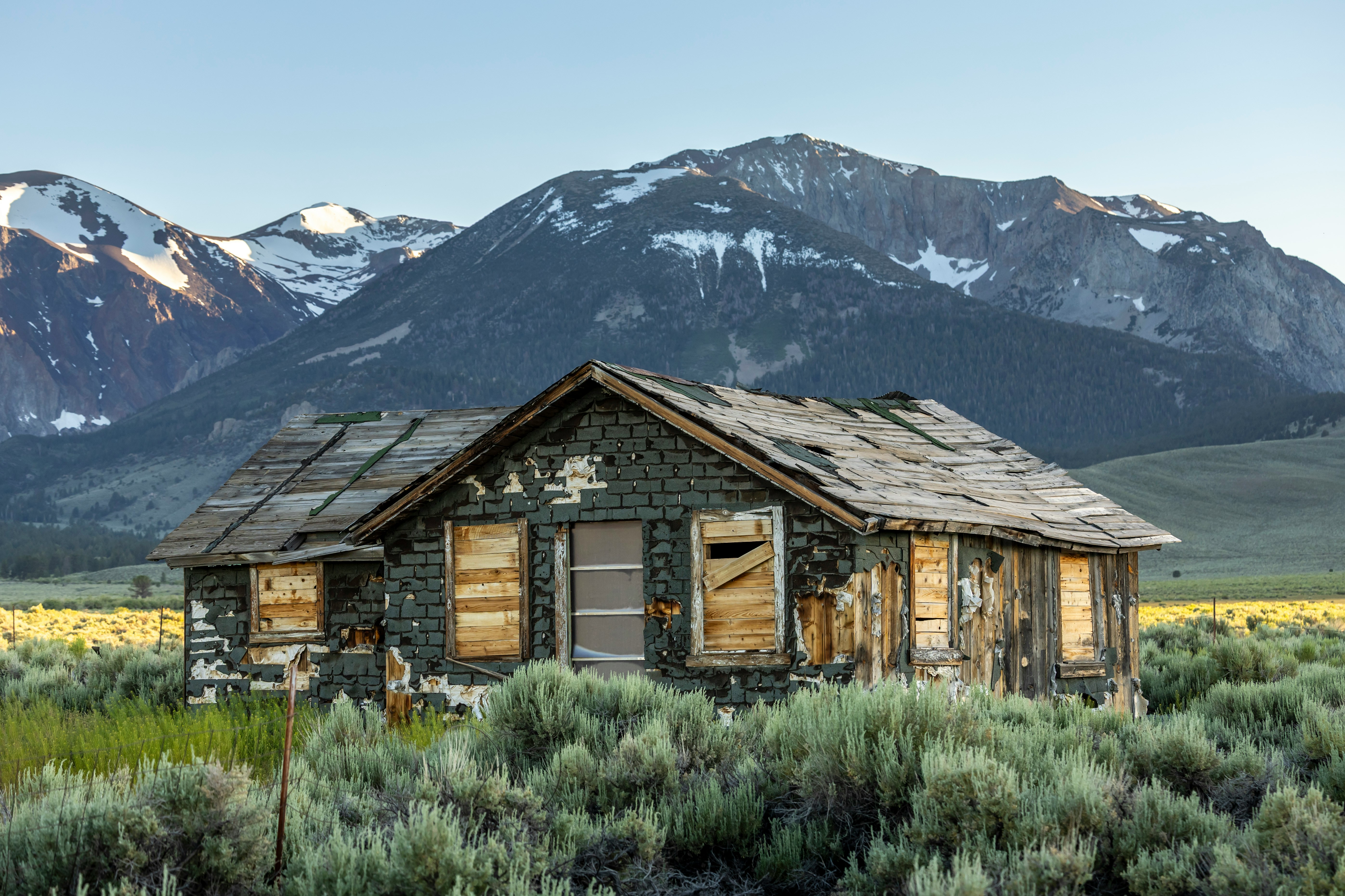 An old abandoned house stands before snow-capped mountains.
