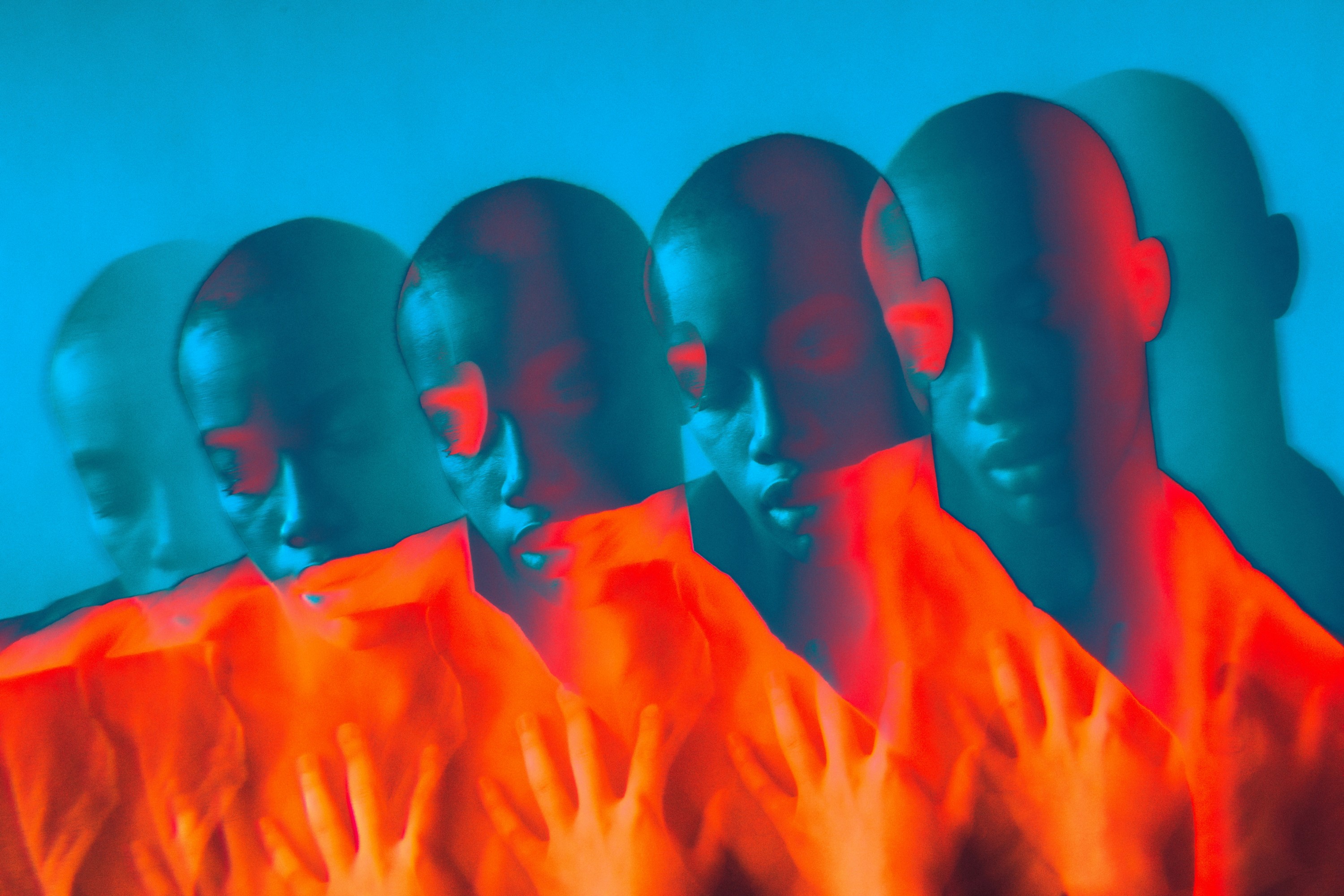 Mehrfach überlagerte Darstellung eines menschlichen Gesichts und von Händen in intensiven Blau- und Rottönen, abstrakte, digital wirkende Lichtkomposition.