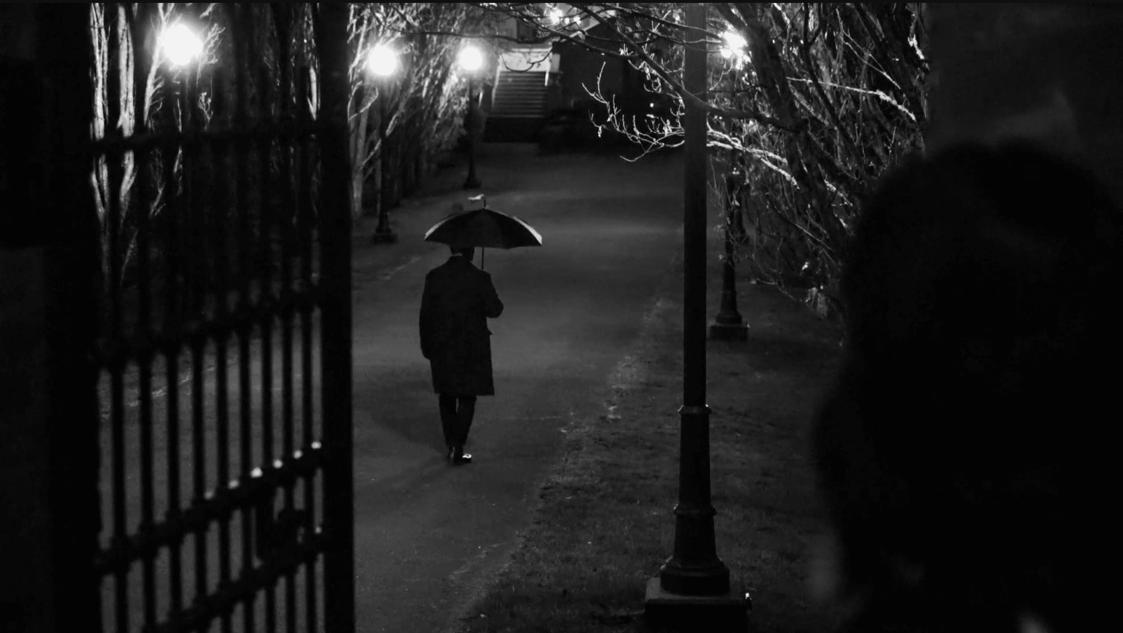 wide shot of someone walking with an umbrella in the evening