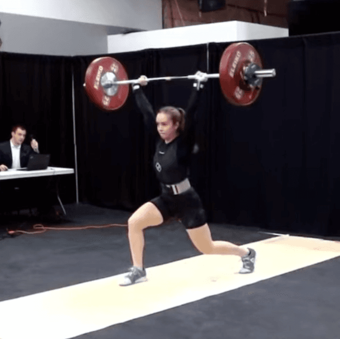 Marie completing a split jerk on a weightlifting platform.