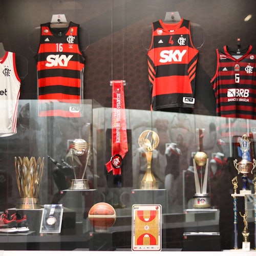 一个展示柜中陈列着弗拉门戈篮球队的球衣、多座奖杯、一个篮球、一条围巾和一个篮球场示意图。