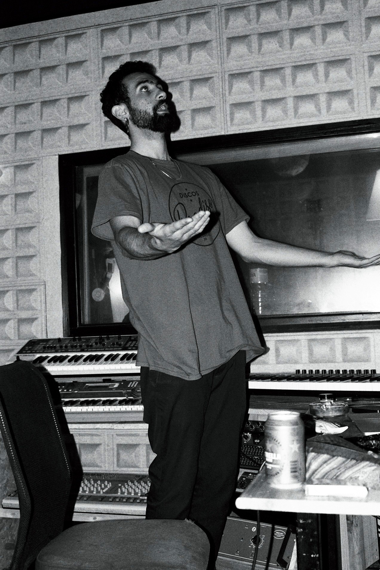 A person in a black and white photo stands near a television, gesturing with one arm in a casual pose.