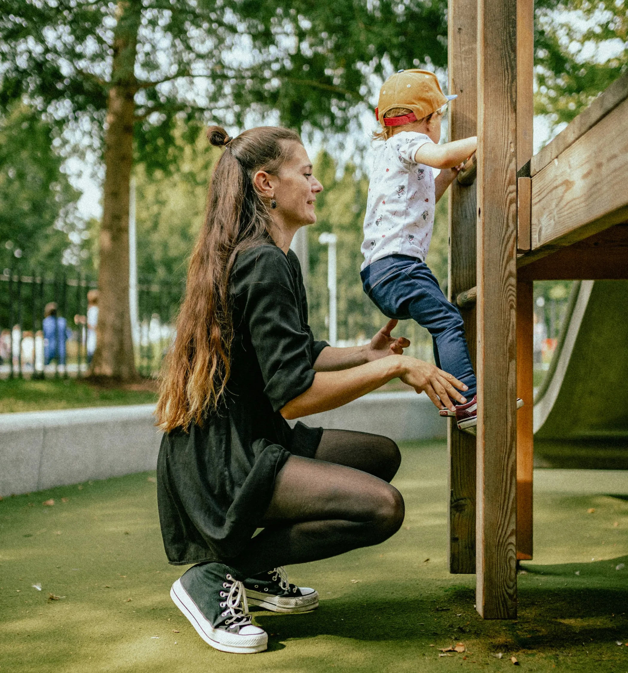 A caregiver smiling while helping a young child climb playground equipment