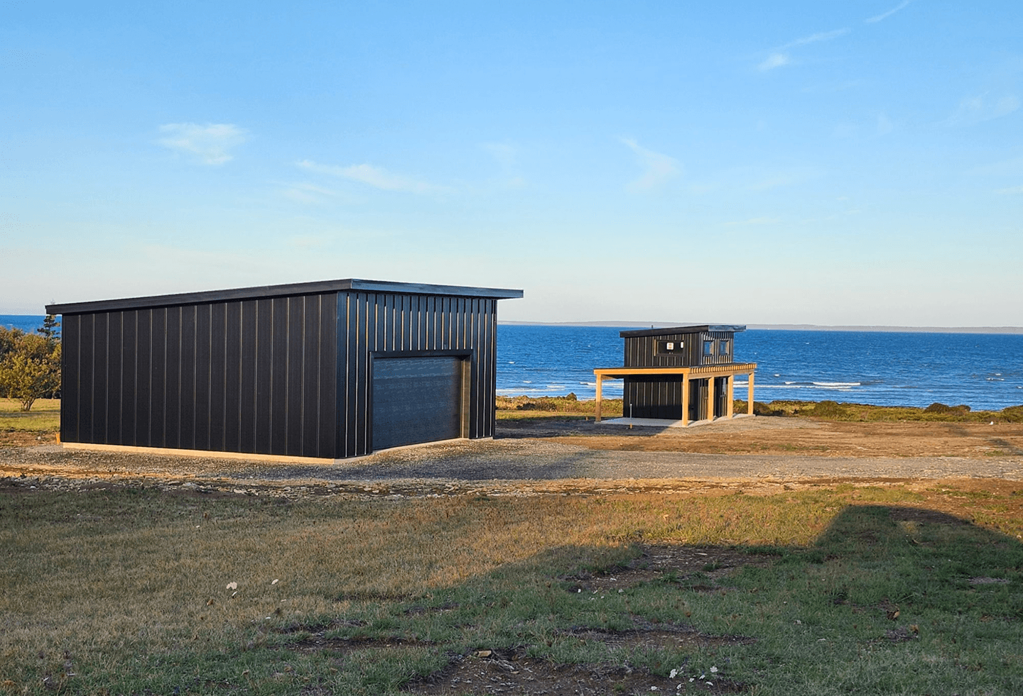 Modern dark-clad building overlooking the ocean under a clear blue sky.