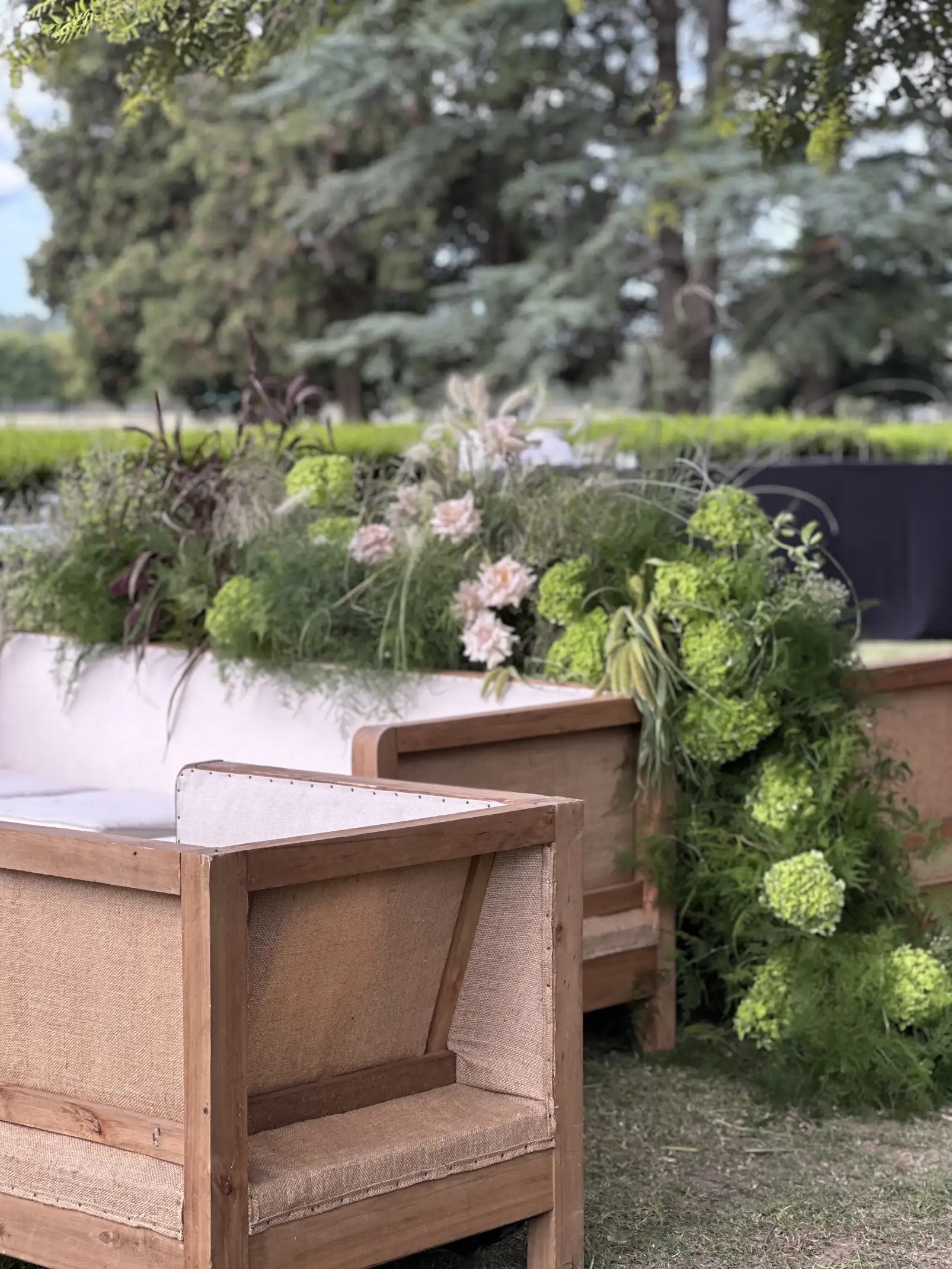 Decoración con flores verdes y rosas detrás de sillones de lino para ambientaciones de boda que mezclan rusticidad y sofisticación.