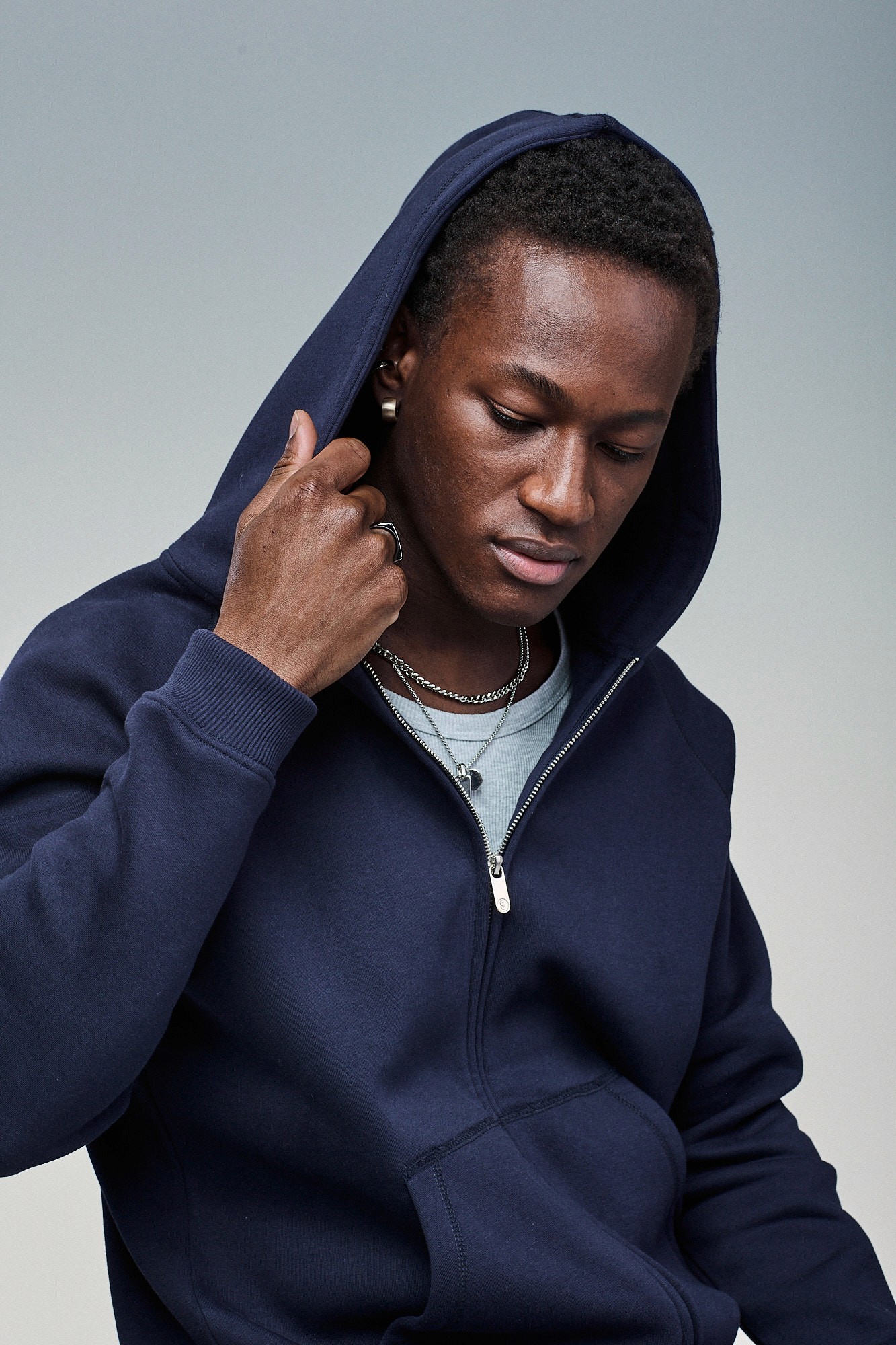Man holding the hood of a Sunday Superior navy zip hoodie, feeling the fabric