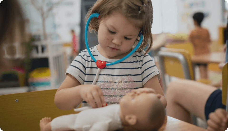 Child engaging in pretend doctor play with a toy stethoscope and doll at Kaleidoscope Kids Booval childcare centre.