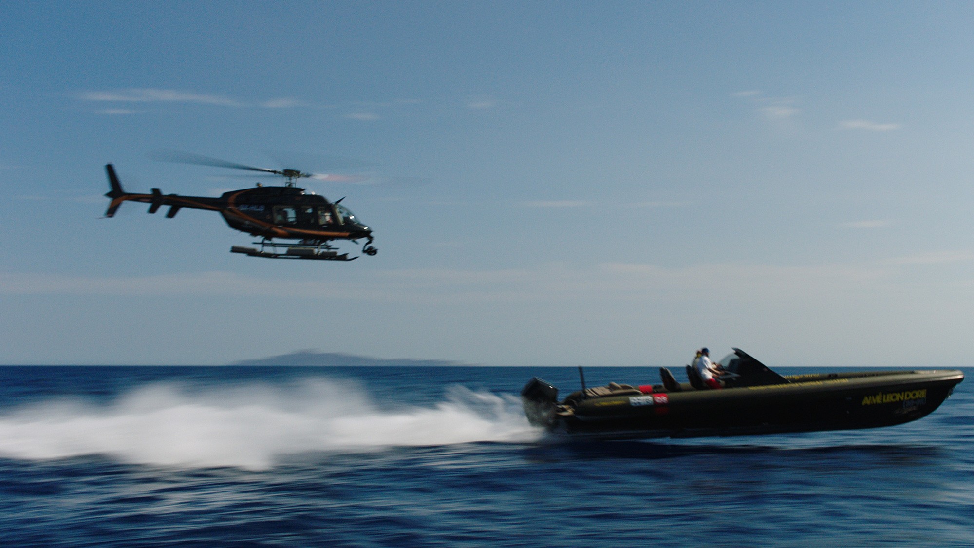 Aimé Leon Dore and Technohull speedboat moving at high speed on open water with a helicopter above