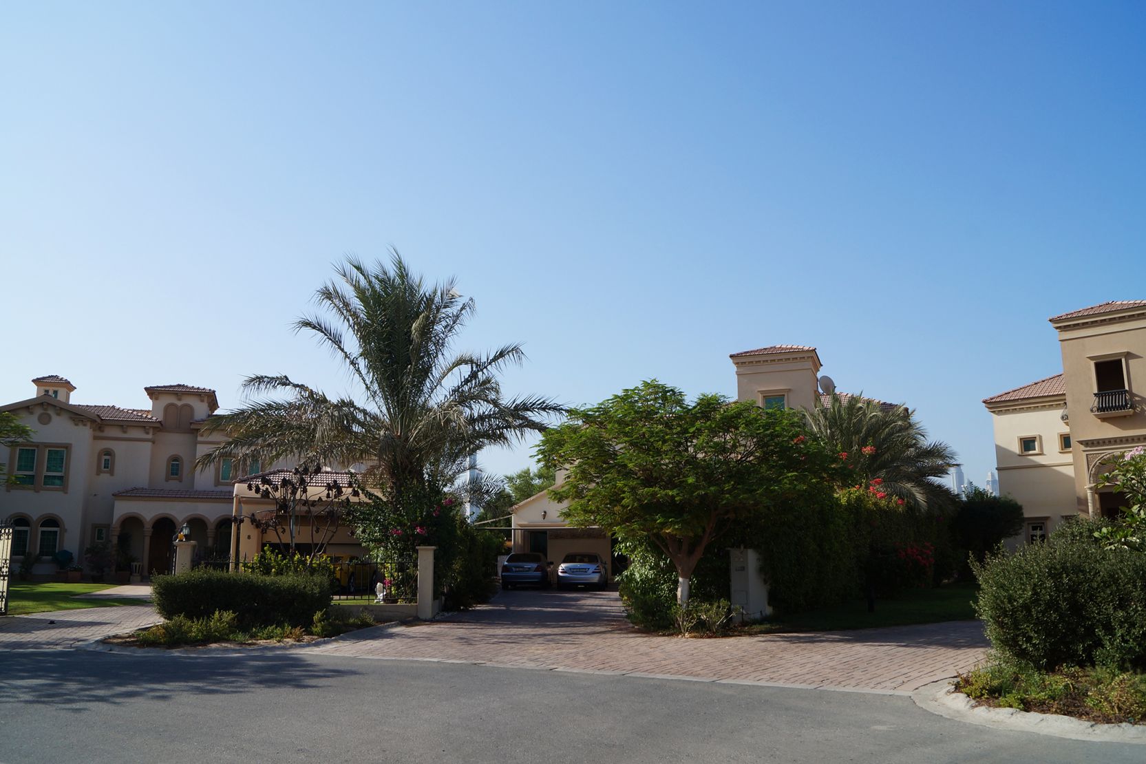 A grand driveway approaches a stunning house, framed by lush palm trees in the prestigious Jumeirah Islands area.