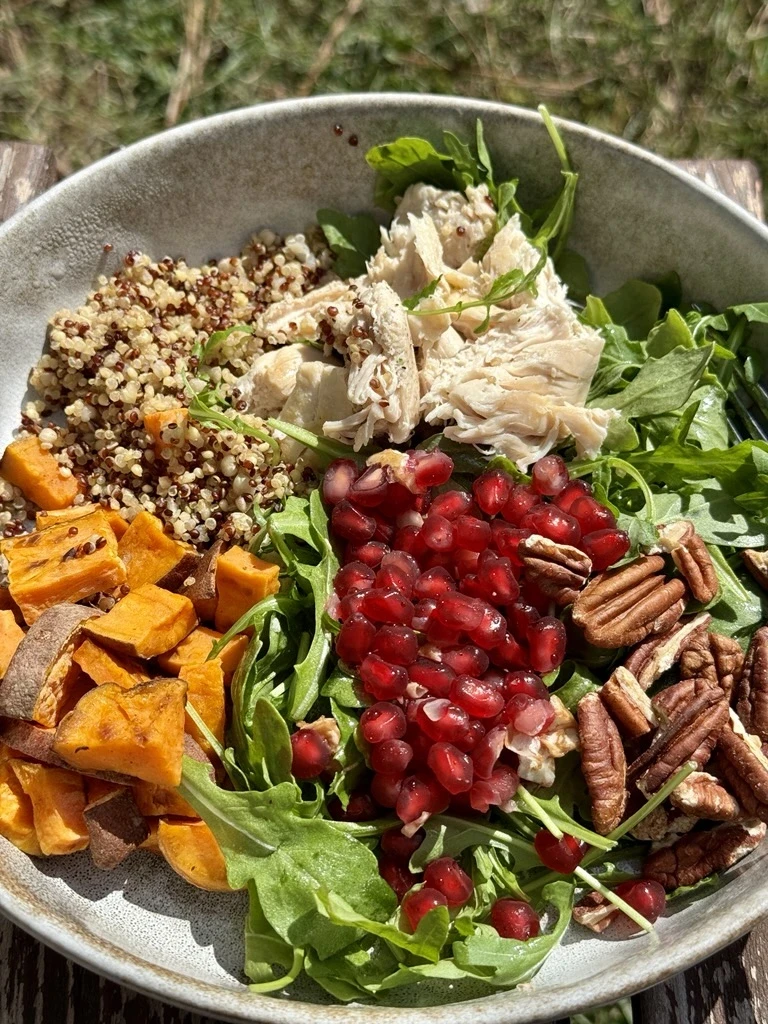 fresh green salad with sweet potatoes, quinoa, chicken, pecans, arugula, and pomegranate arils