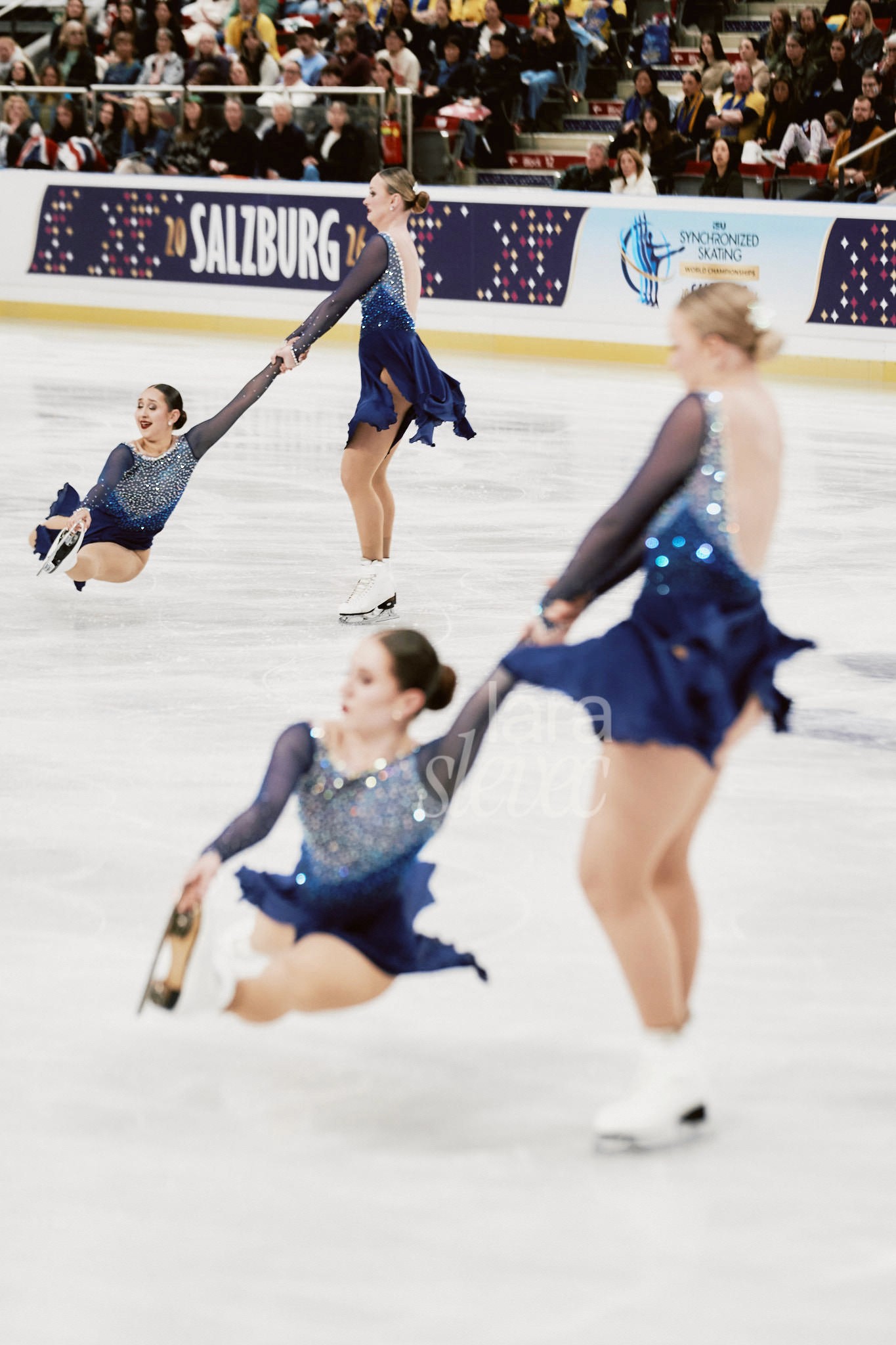 Zwei Synchroneiskunstlaufpaare bei einer Variation der Death Spiral im Spagat. Team Skyliners. ISU Synchronized Skating Championships 2026 in Salzburg. Fotografiert von Lara Slevec.