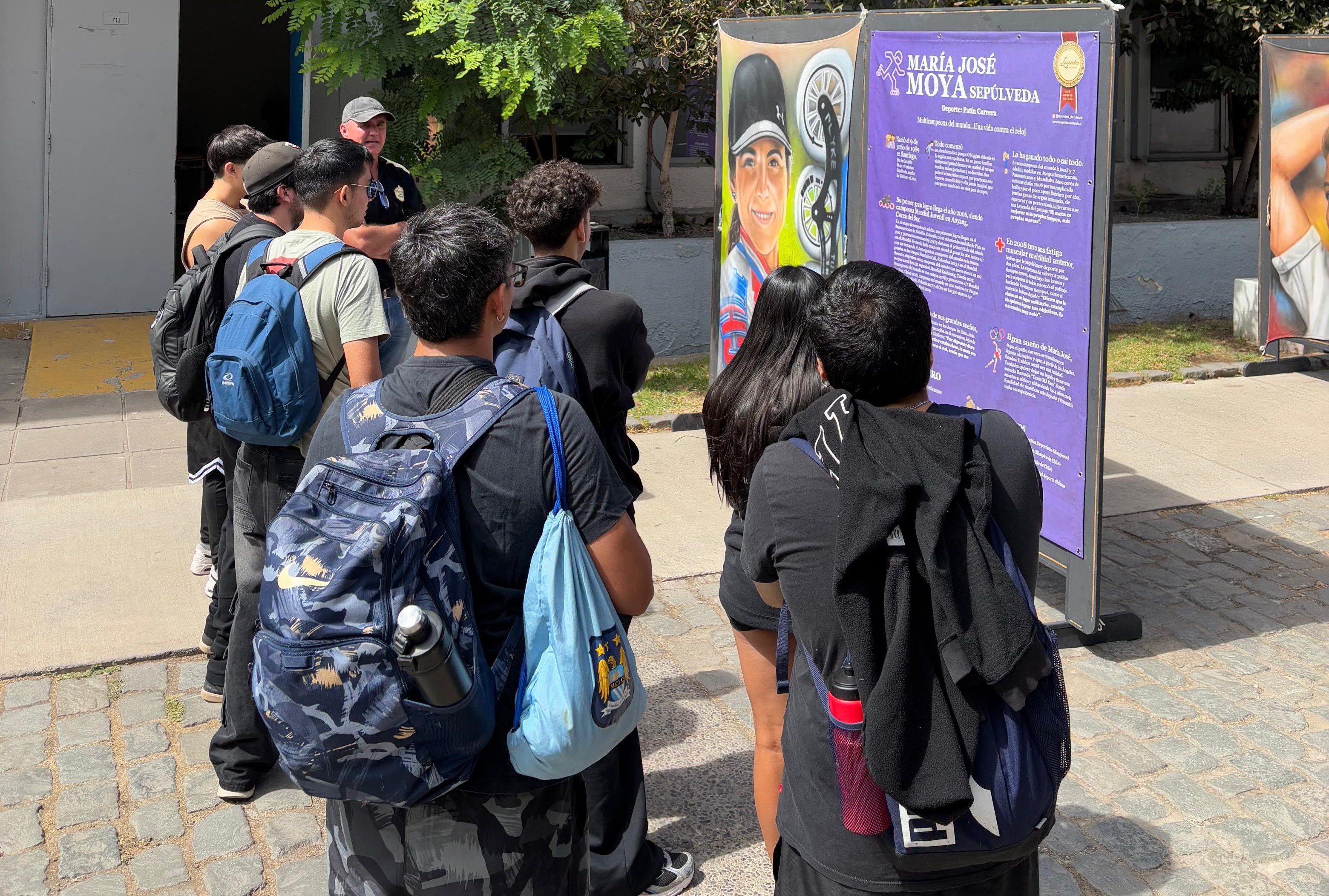 Visitantes en la exposición Leyendas del Deporte admirando la pintura de María José Moya, patinadora chilena de velocidad.