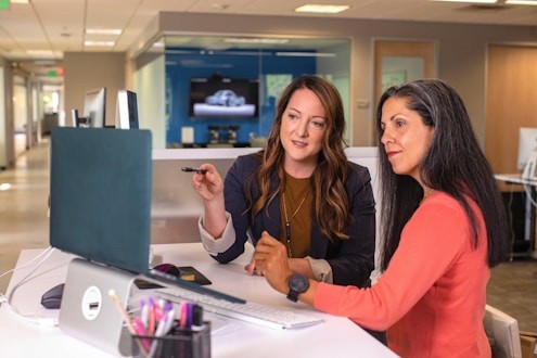 Two professionals working at a computer in a shared workspace.