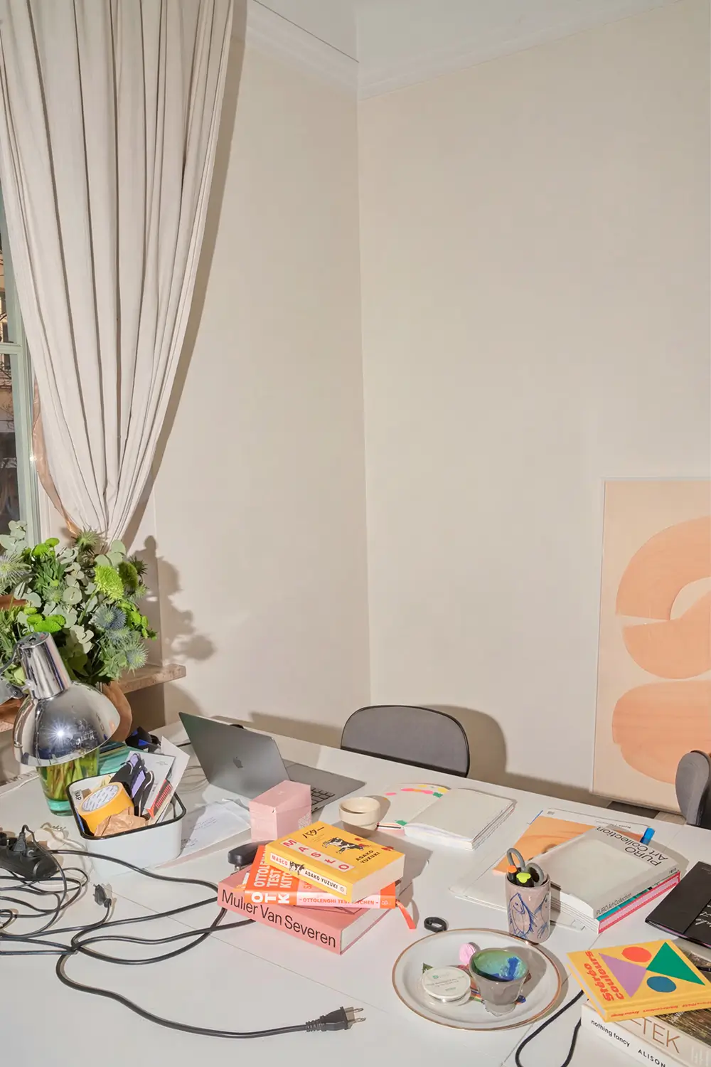 Bright desk in a design studio with a laptop, design books, and accessories.