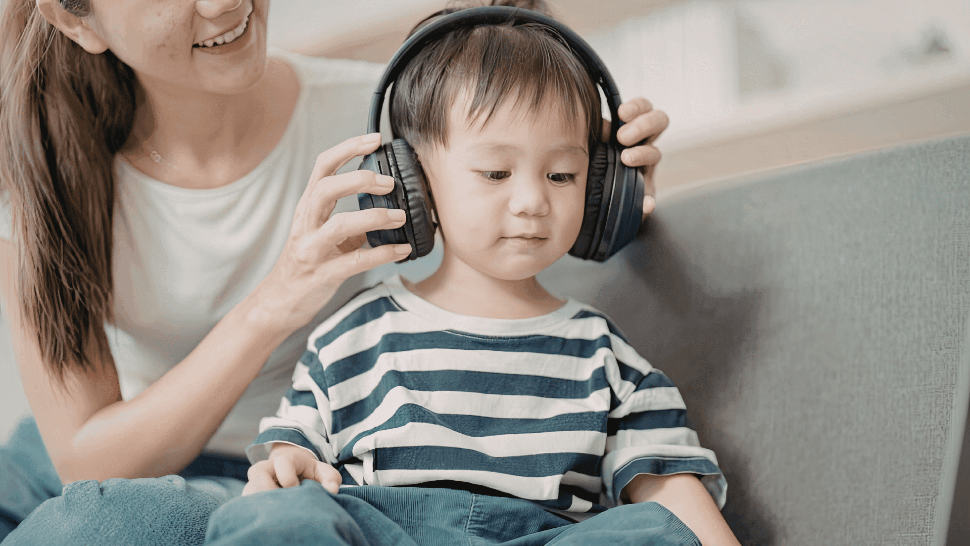 A mother and son sitting on a sofa, with the mother placing headphones on her child as they get ready to listen to HushAway®’s Sound Sanctuary.