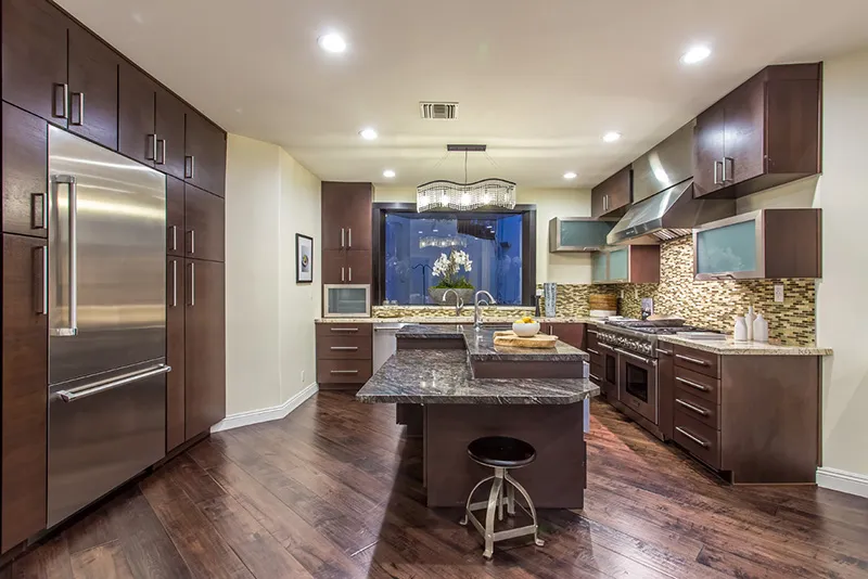 Aerial view of a small neighborhood with red-roofed houses nestled among lush green fields and winding roads. The scene feels peaceful and idyllic.