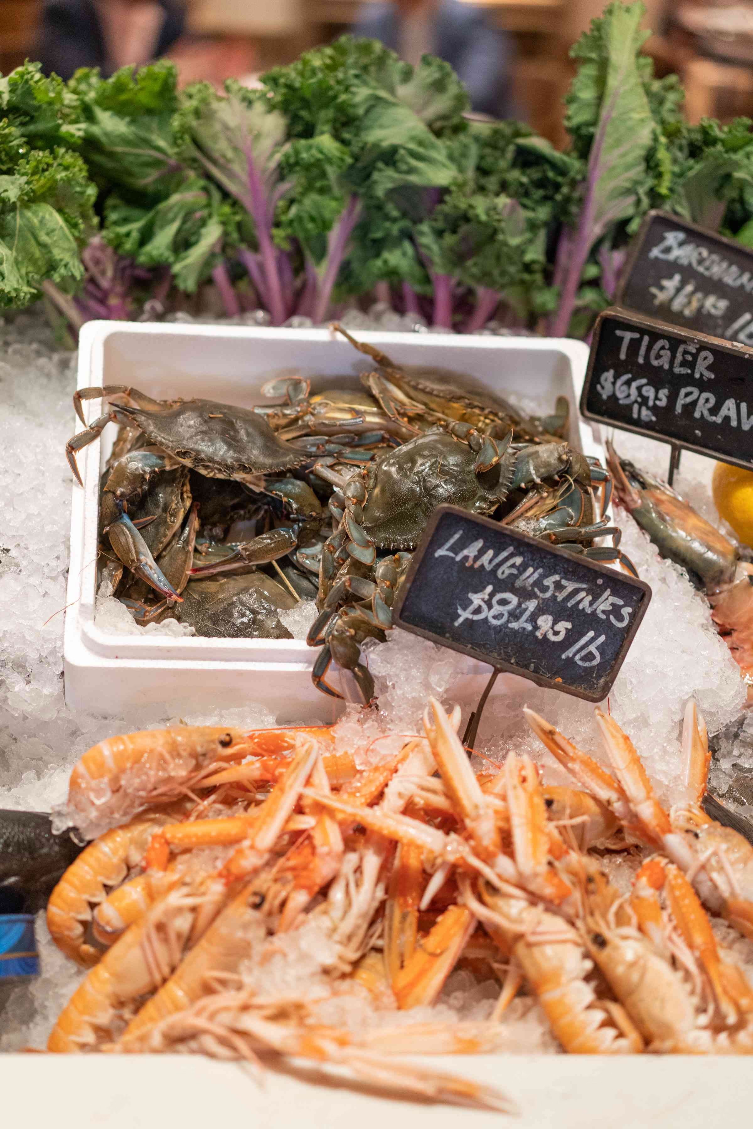A variety of fresh seafood displayed at a market, including shrimp and seaweed, with a chalkboard label.