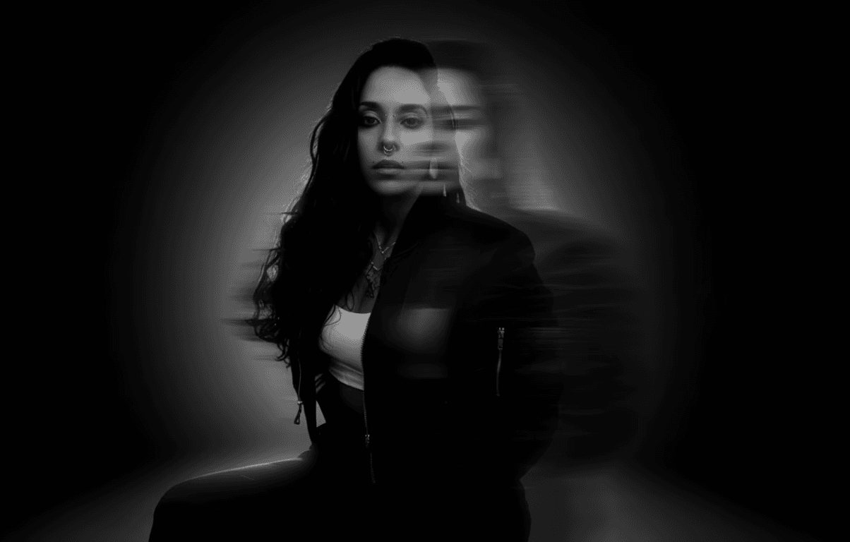 A thoughtful young person with dark hair gazes to the side, captured in soft black and white lighting.