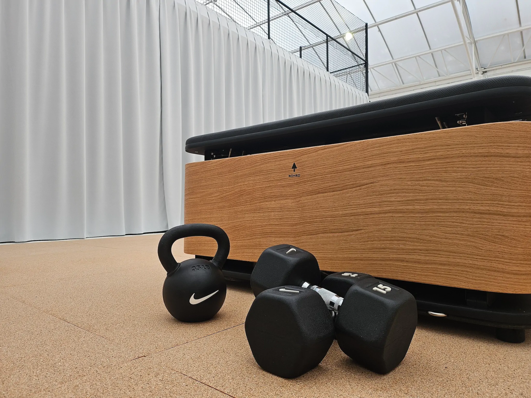 Haltères et kettlebell noirs devant équipement de musculation en bois. Idéal pour séance de sport.