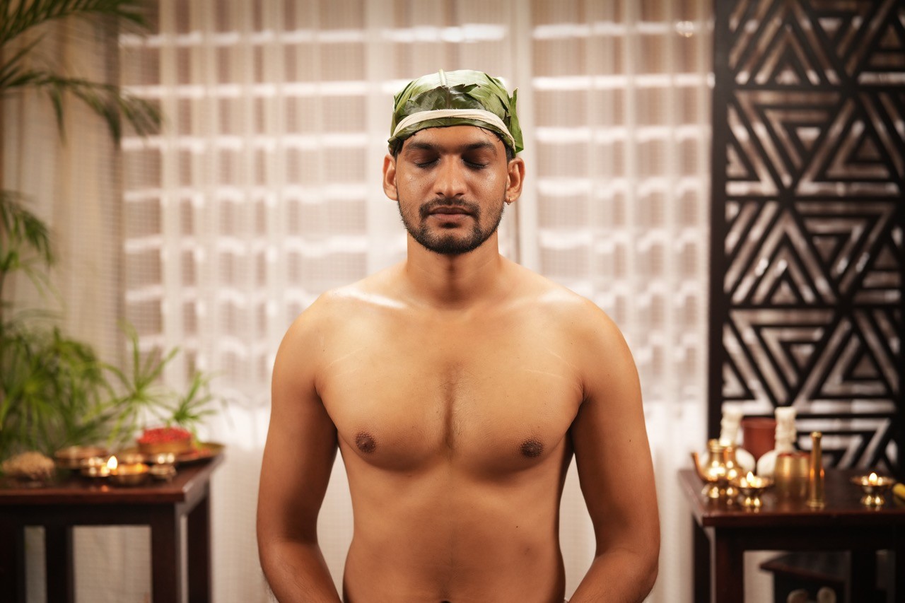 Ayurvedic therapy for sinusitis and migraines – A man with a herbal leaf band around his forehead, meditating in a peaceful wellness setting, promoting holistic healing and relaxation at au revoir resort