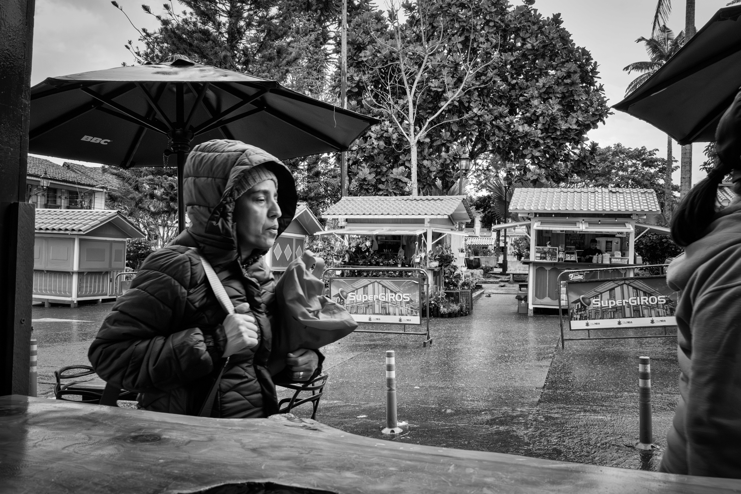 Rainy street scene with people passing by a bar window.