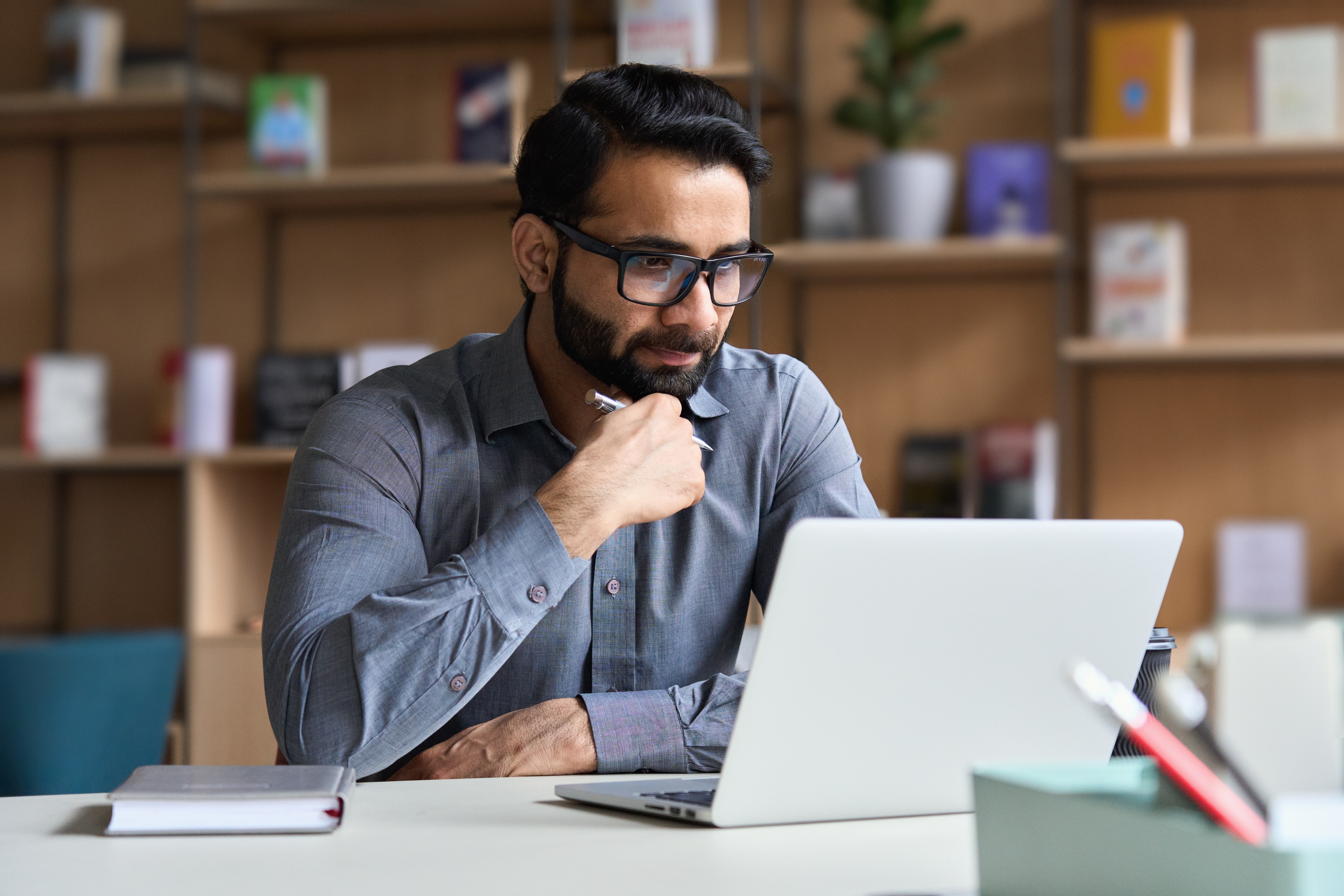 Professional male remote employee in a grey shirt, deeply focused on his laptop, symbolising dedicated offshore workforce solutions for UK companies seeking productivity and cost savings.