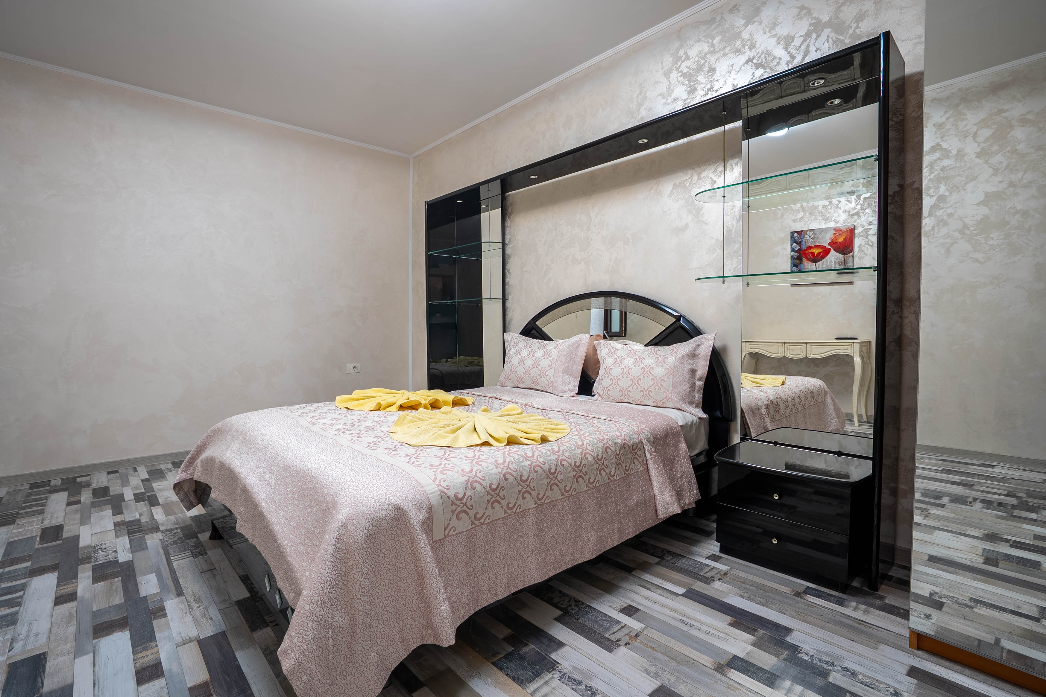A modern hallway features vibrant teal and orange geometric and leaf patterns, with glossy tiled floors, a large rectangular light fixture, and a small shelf holding a potted plant, all leading to a large, frosted window at the end.
