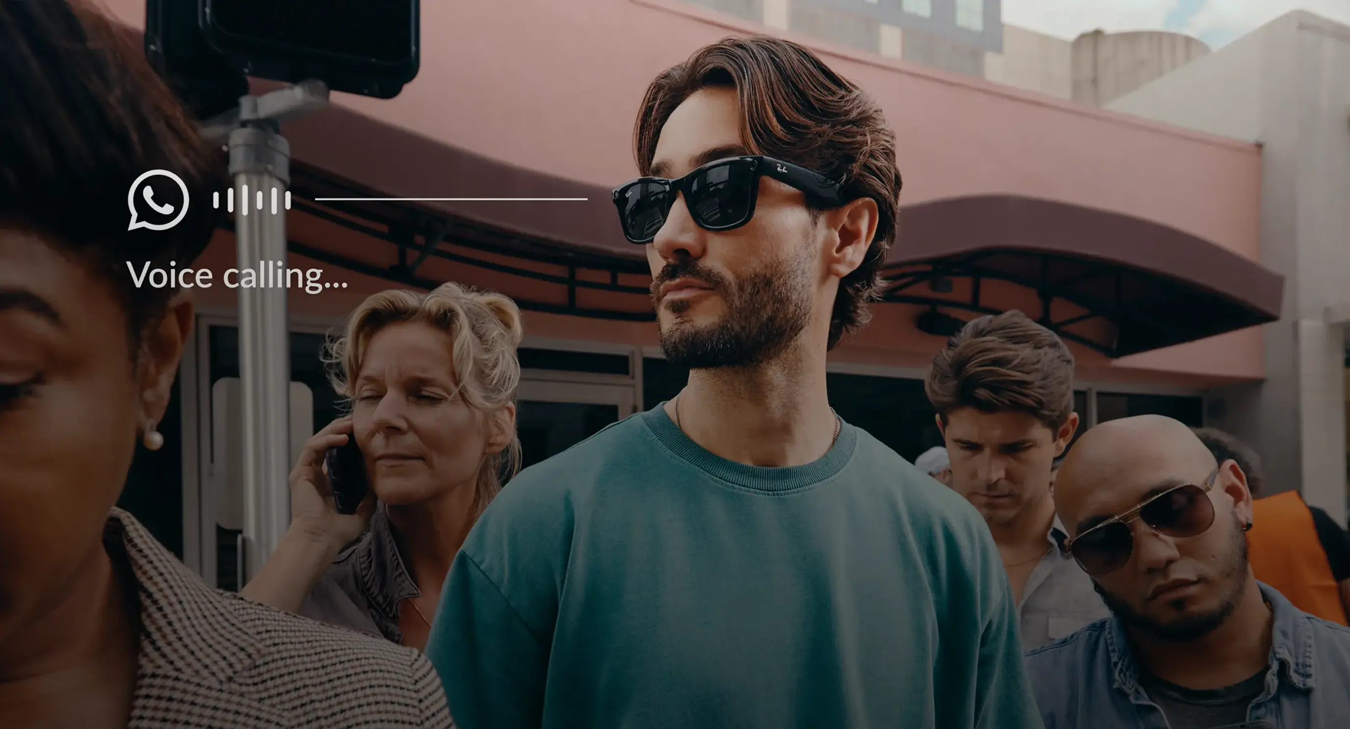 A man wearing Ray-Ban Meta smart glasses makes a hands-free WhatsApp voice call in a crowded outdoor setting. A "Voice calling..." indicator with the WhatsApp logo overlays the image, showing audio output without earbuds or a phone in hand.