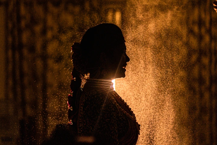 Candid silhouette of Harshitha in traditional attire against glowing light. Captured by Out of The Blues Fine Art Wedding Photography in Hyderabad.