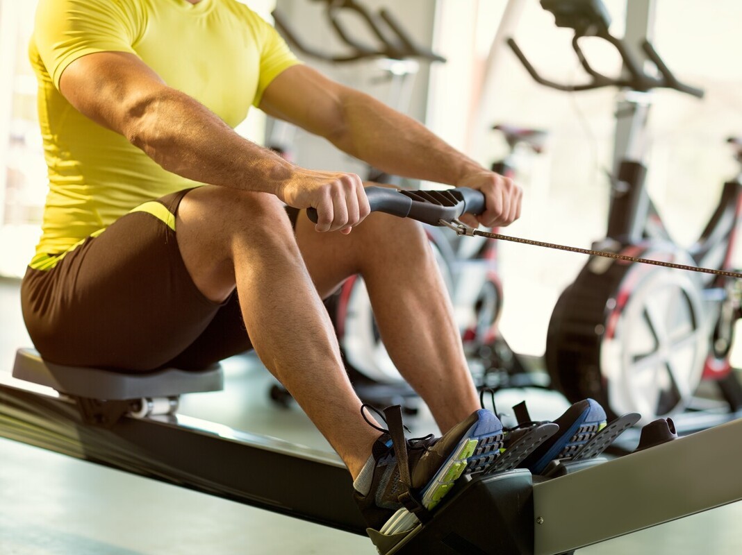 man using a rowing machine in a gym for cardio alongside his running plan for weight loss