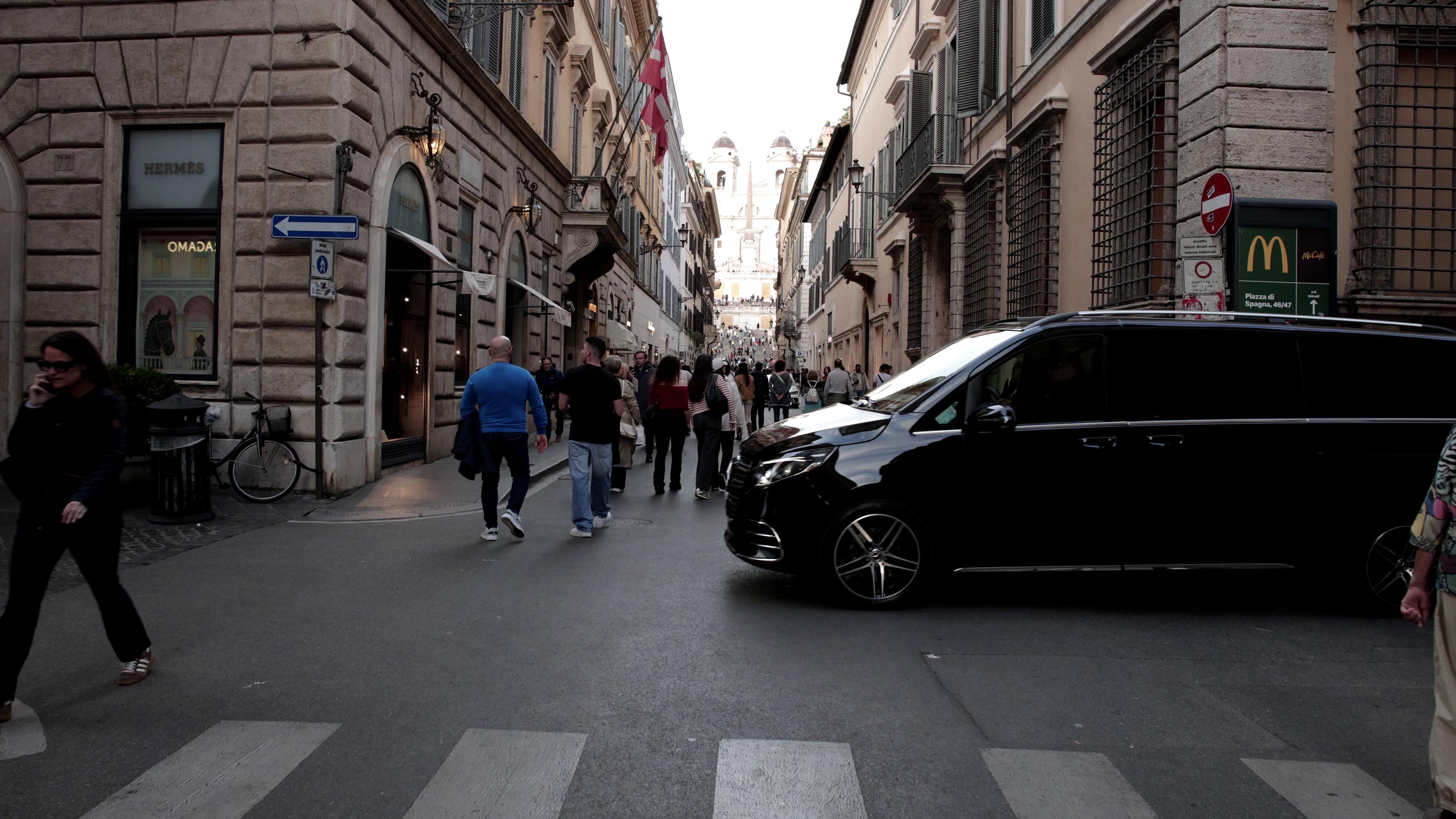 A Mercedes van passting in front of a crowd passing through the Spanish Steps.