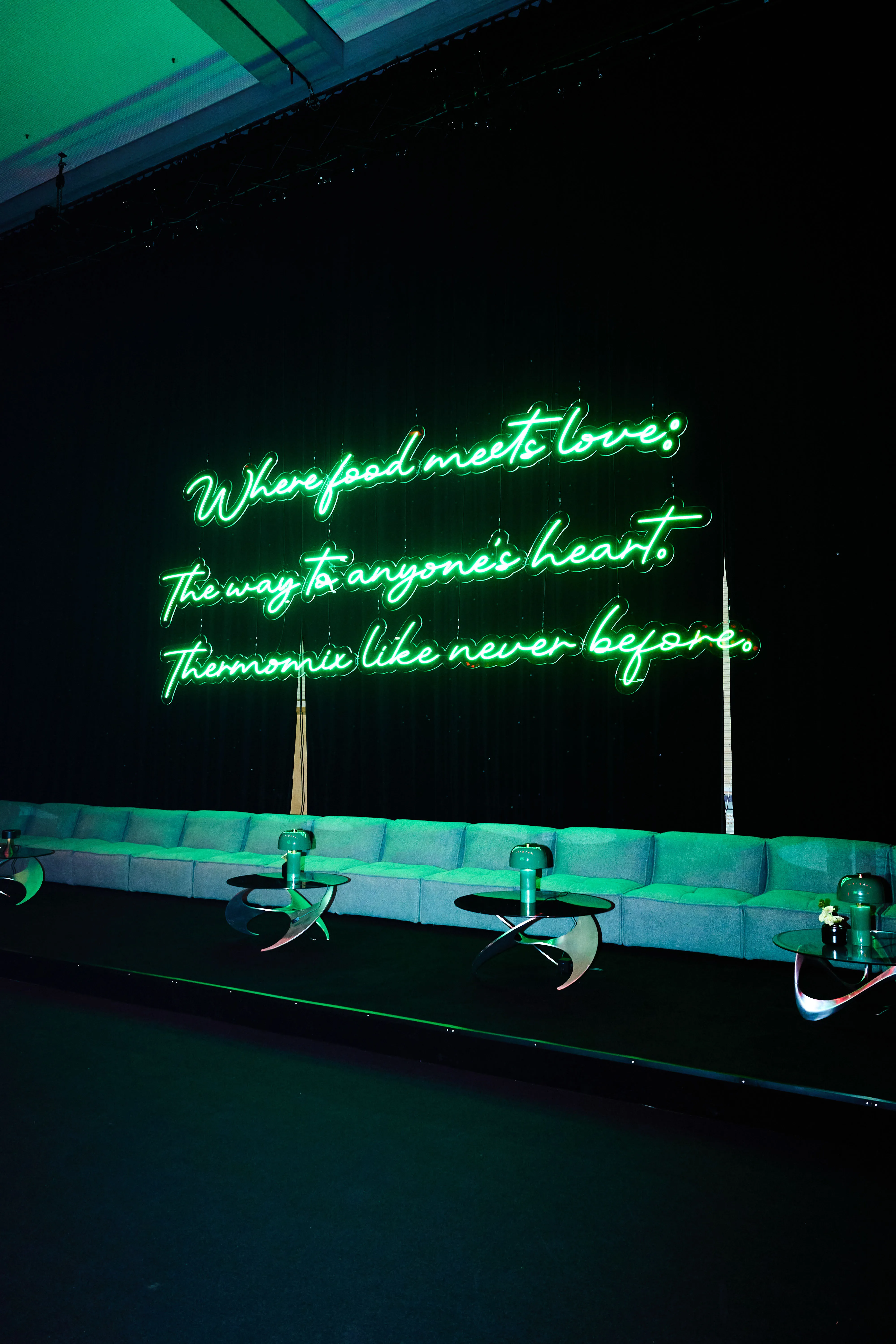 Green neon slogan Where food meets love above a long sofa with snack tables.