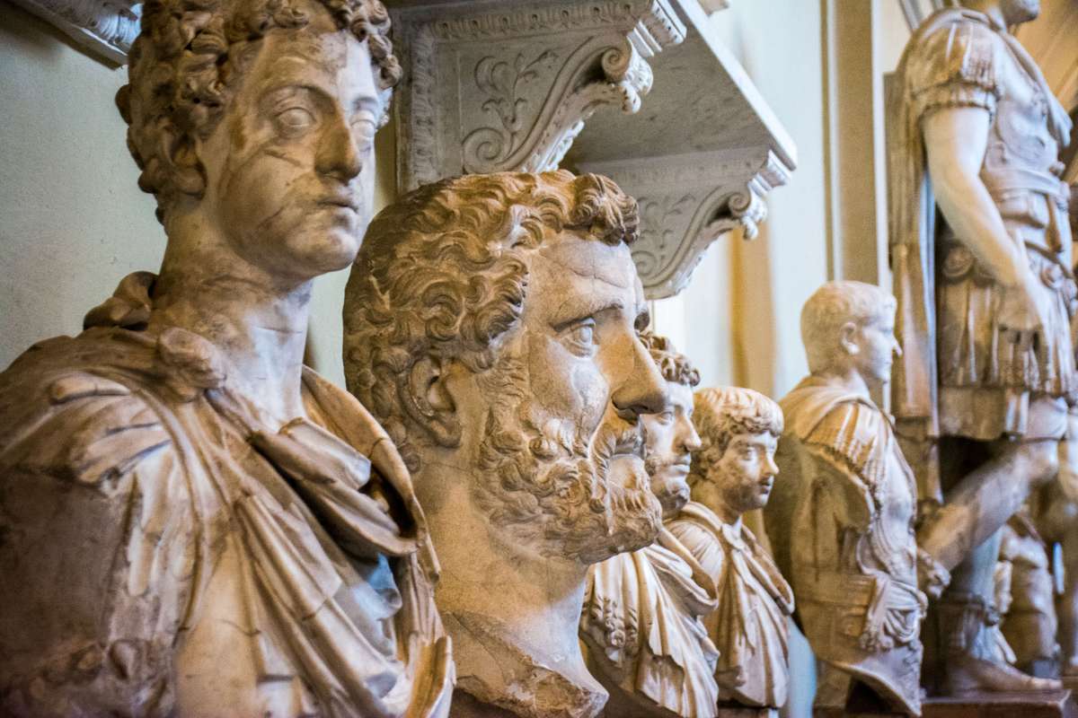 A row of marble classical sculptures and busts displayed in a museum gallery with ornate architectural details.