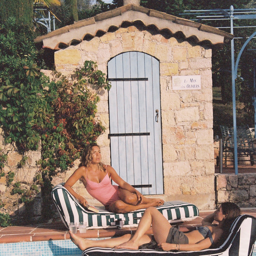Woman relaxing poolside on a luxury green-and-white pool float at a Mediterranean villa with stone pool house