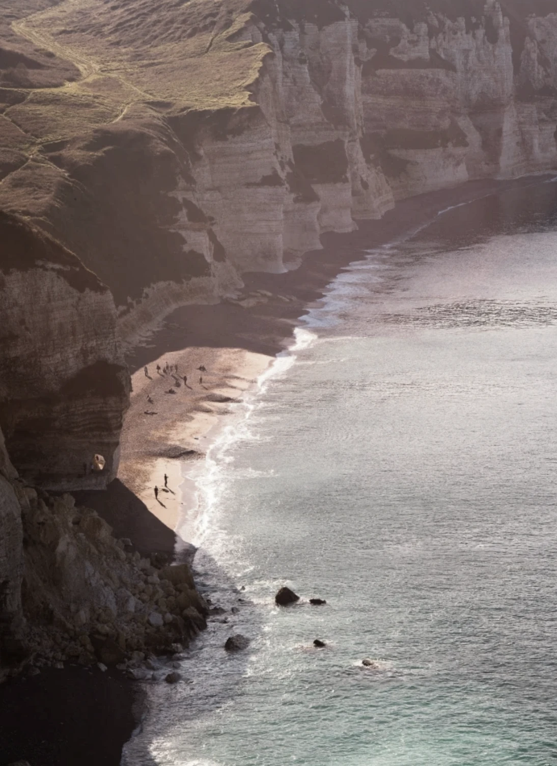 Steep white cliffs meeting the sea at low tide, with tiny figures walking along the shore below.