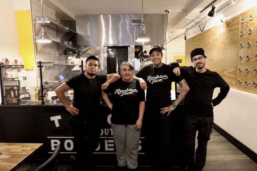 Revolution Taco team members standing together inside the restaurant kitchen, wearing black Revolution Taco shirts.