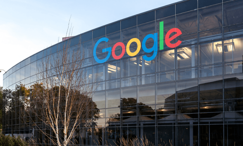 The Google logo is prominently displayed on a sleek glass building, framed by trees, with reflections of surrounding buildings and trees creating a vibrant scene.