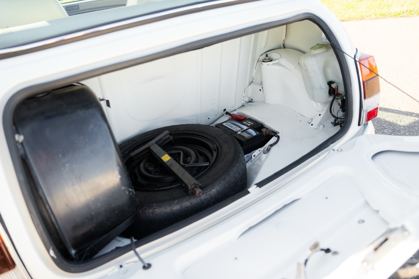 A close-up of a small, clear hatch on a white vehicle, revealing a black seat and control panel inside.