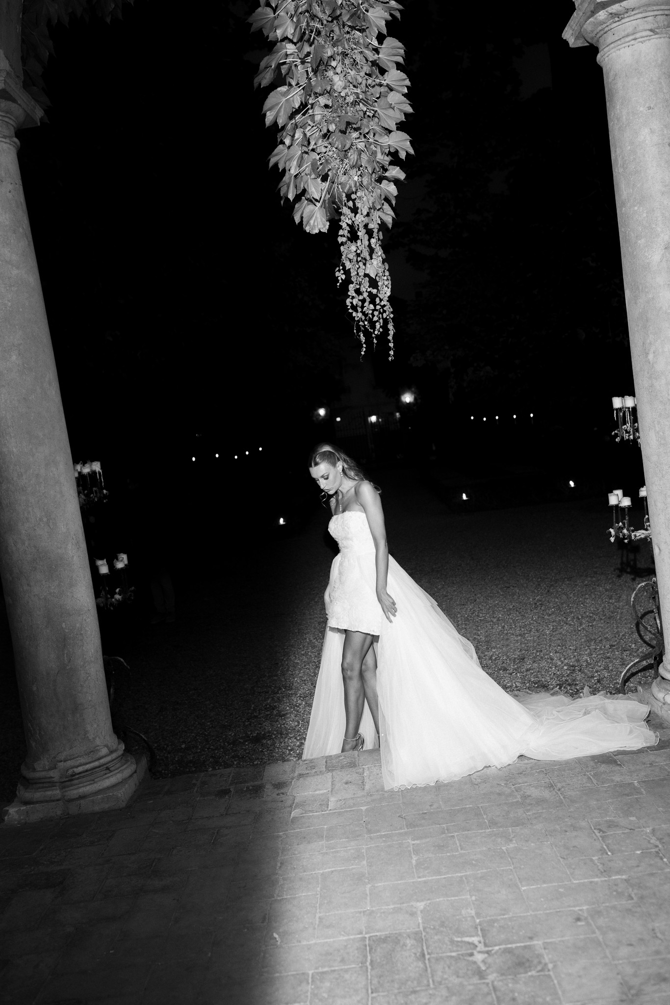 Sposa in abito bianco sotto il loggiato notturno di Villa Ferrari, tra colonne e decorazioni floreali sospese