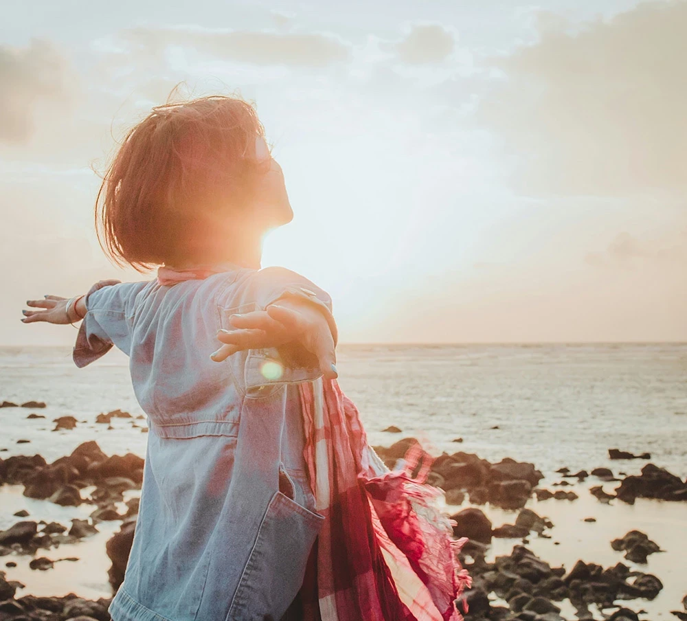 woman looking out to sea during a sunsetwith her arms held out wide