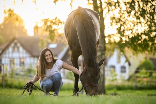 Adriana lacht in die Kamera und berührt ein Pferd liebevoll am Kopf.