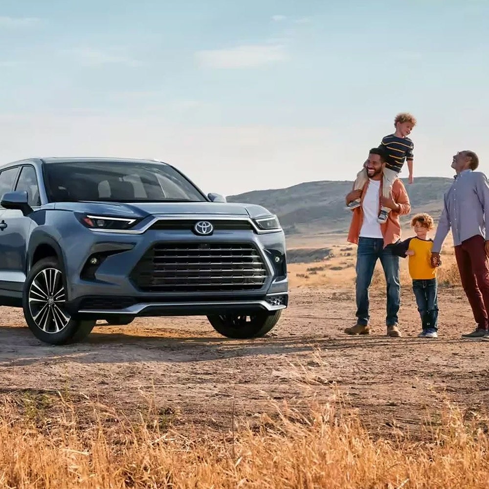 A family of two dads and two children walking towards a 2025 Toyota Grand Highlander.